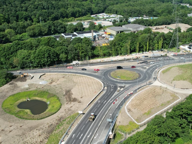 Cars driving around the new roundabout with the new bridge in the foreground.